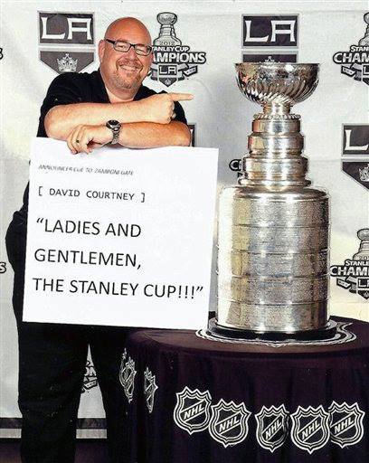 David Courtney holding a sign saying "Ladies and gentlemen the Stanley Cup. David is standing right next to the Stanley Cup after the LA Kings won the cup.